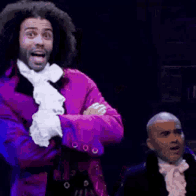 a man in a purple jacket and white gloves is standing in front of a man in a tuxedo .