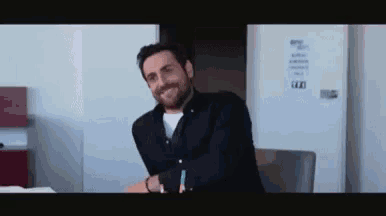 a man with a beard is smiling while sitting at a desk in a room .