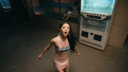 a woman in a pink dress stands in front of a vending machine that says ice