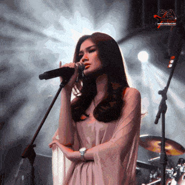 a woman singing into a microphone with a watch on her wrist in front of a drum set