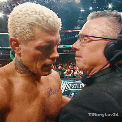 a man with a tattoo on his chest talks to another man in front of a sign that says wrestle on it