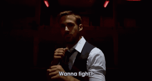 a man in a suit and tie is standing in a dark room and says wanna fight .