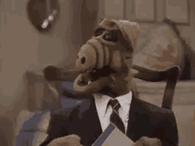 a stuffed animal in a suit and tie is sitting in a chair .
