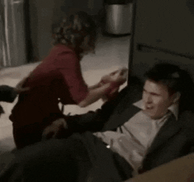 a man in a suit is laying on the floor while a woman holds his hand .