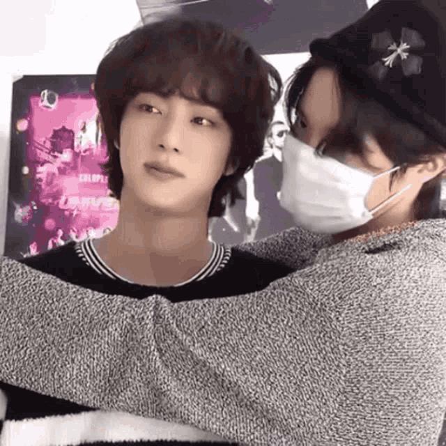 a man wearing a mask is hugging another man in front of a poster that says colorful universe
