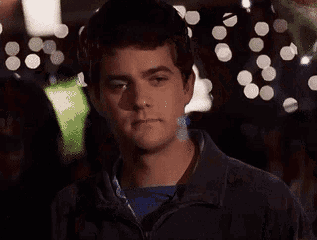 a man with his eyes closed is standing in front of a blurry background of christmas lights .