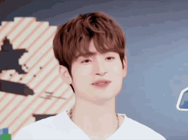 a young man with brown hair is wearing a white shirt and a necklace