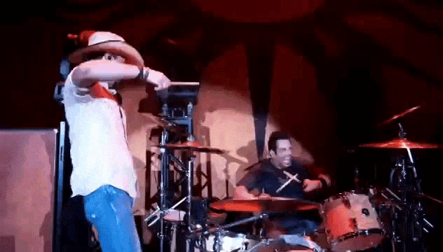 a man in a cowboy hat is standing on a stage playing drums .