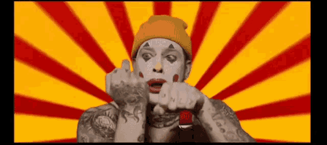 a man with a clown makeup on his face and a yellow hat is giving the middle finger .