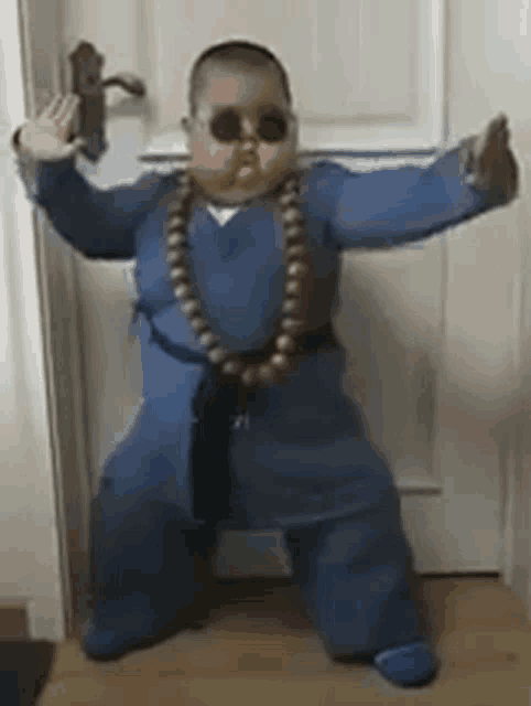 a baby is wearing sunglasses and a necklace and is dancing in front of a door .