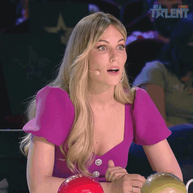 a woman in a purple top is sitting in front of a microphone and the word talent is on the screen behind her