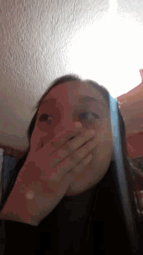 a woman covering her mouth with her hands while looking at a phone
