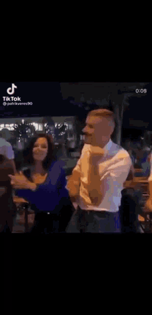 a man in a white shirt is dancing with a woman in a blue shirt at a party .