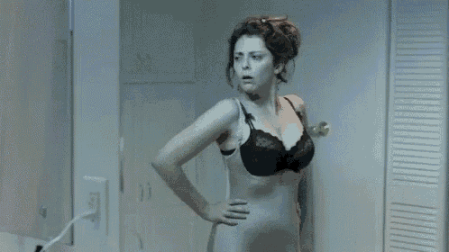a pregnant woman in a black bra is standing in front of a mirror in a bathroom .