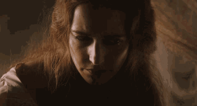a woman with long red hair looks down at something