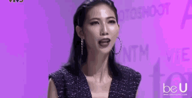 a woman is standing in front of a purple wall with the words beu academy written on it .
