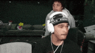 a man wearing headphones is sitting in front of a couch while another man looks on .