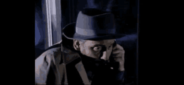 a man in a hat and trench coat is talking on a phone .
