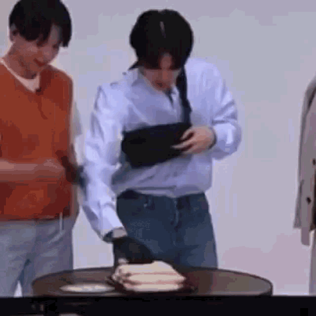 a man is standing next to a table with a plate of food on it and holding a black bag .