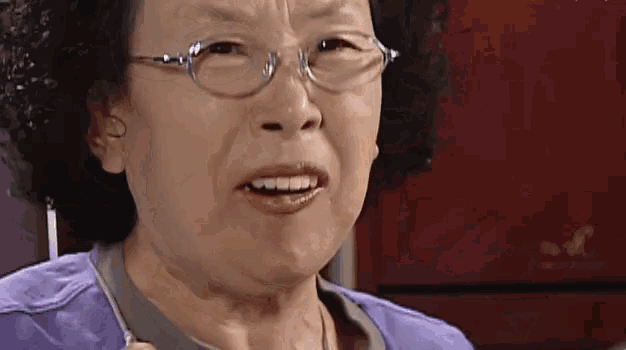 a close up of a woman wearing glasses and a purple shirt making a funny face .