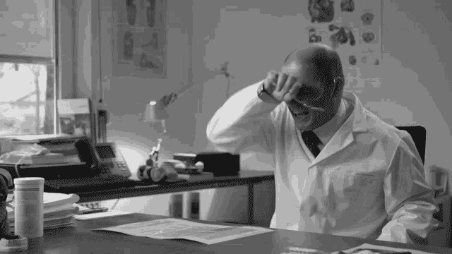 a man in a lab coat is sitting at a desk with his hand on his head