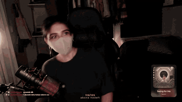 a woman wearing a face mask is sitting in front of a microphone and a screen that says swing for me