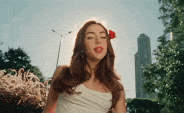 a woman in a white dress with a red rose in her hair is standing in front of a tall building .
