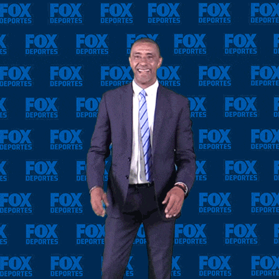a man in a suit and tie is standing in front of a fox deportes wall