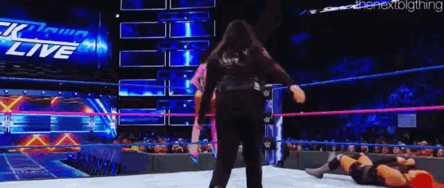 a woman is standing in a wrestling ring next to a man laying on the ground .