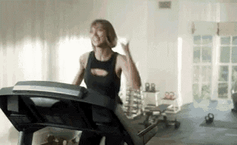 a woman is running on a treadmill in a gym while holding a cell phone .