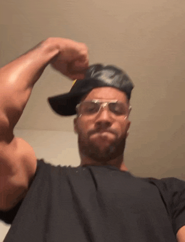 a man wearing a hat and sunglasses is flexing his arm