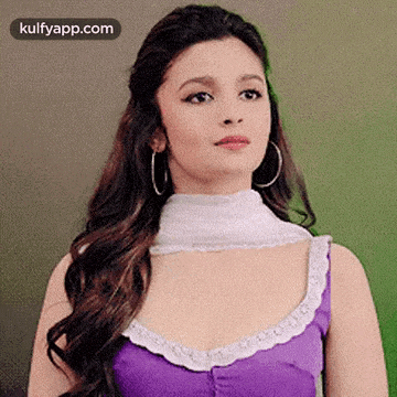 a woman wearing a purple top and hoop earrings is standing in front of a green wall .