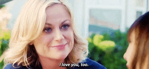 a woman is smiling at another woman and saying `` i love you , too '' .