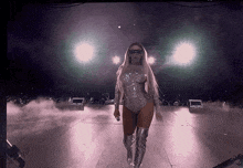 a woman in a bodysuit and thigh high boots is walking on a stage .