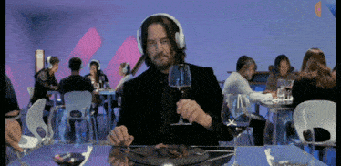 a man wearing headphones sits at a table with a plate of food and a glass of wine