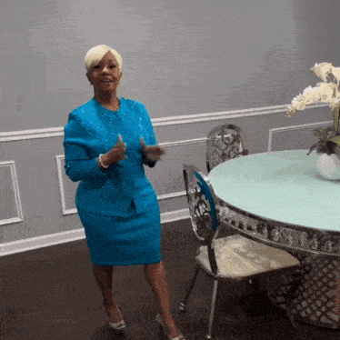 a woman in a blue suit stands in front of a table and chairs