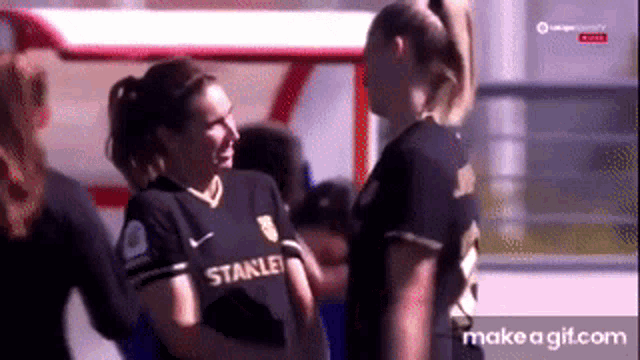 two women are standing next to each other on a soccer field .