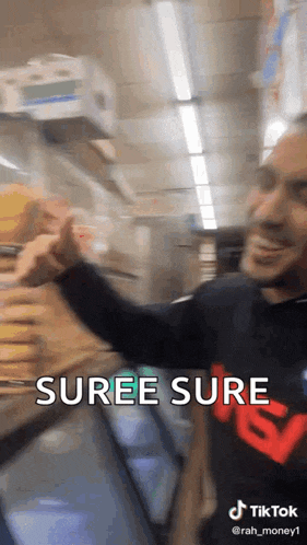 a man in a black shirt with the word suree sure on it is standing in front of a refrigerator in a store .