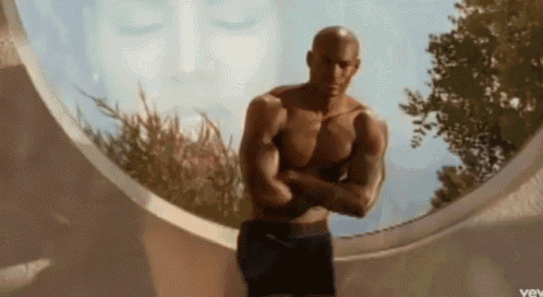 a shirtless man with his arms crossed is standing in front of a window