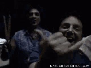 a man is making a funny face in a dark room while holding a cigarette .
