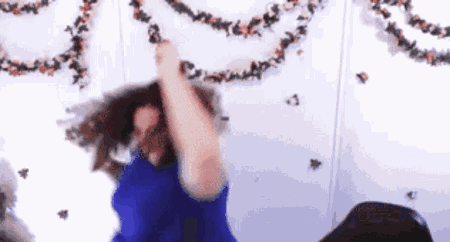 a woman in a blue dress is dancing in front of a white wall with christmas garland hanging on it .