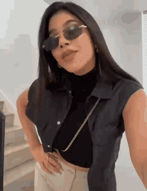 a woman wearing sunglasses and a black shirt is standing in front of stairs .