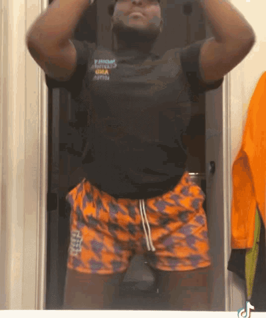 a man in a black shirt and orange shorts stands in front of a door