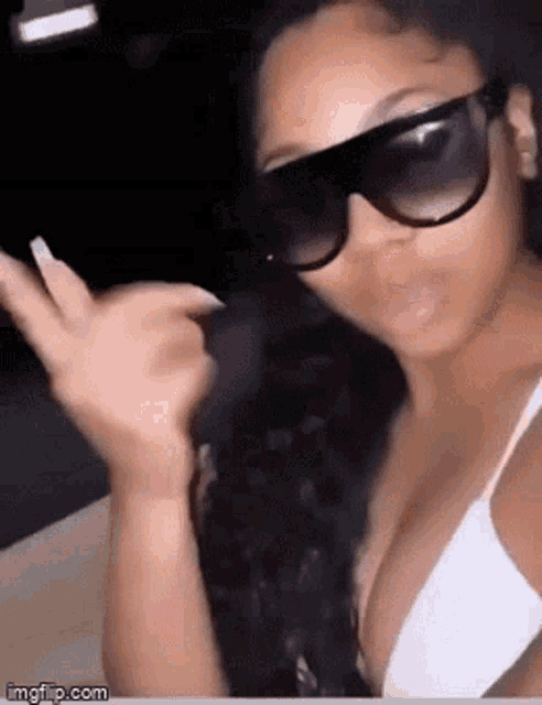 a woman wearing sunglasses and a white bra is making a funny face .
