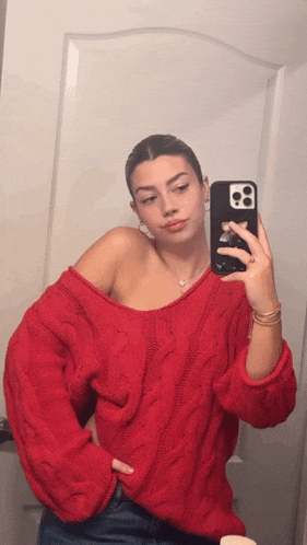 a woman in a red sweater is taking a picture of herself in a mirror