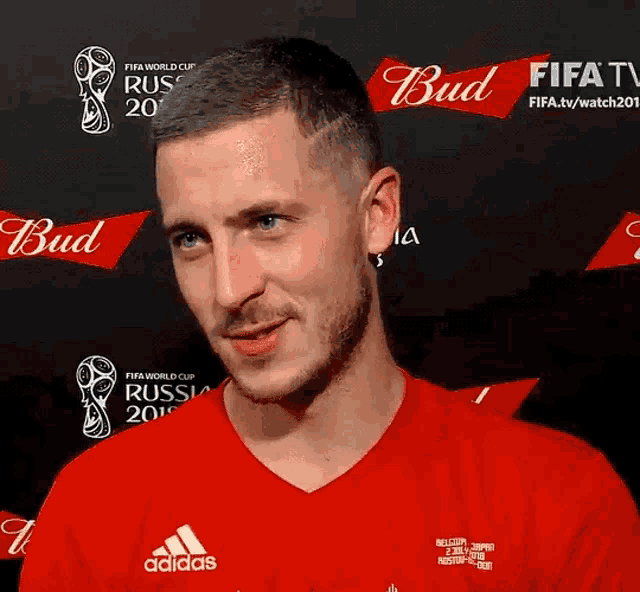a man wearing a red adidas shirt stands in front of a bud advertisement