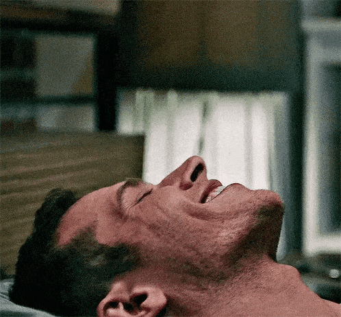 a shirtless man is laying on a bed with his eyes closed and his mouth open .