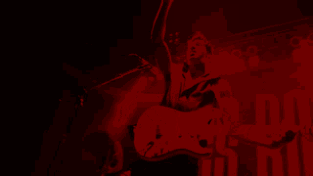 a man playing a guitar in a dark room with a red background