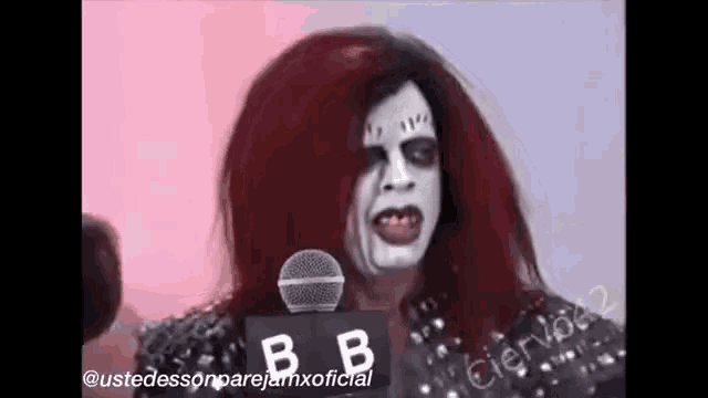 a person with red hair and white paint on their face is standing in front of a microphone .
