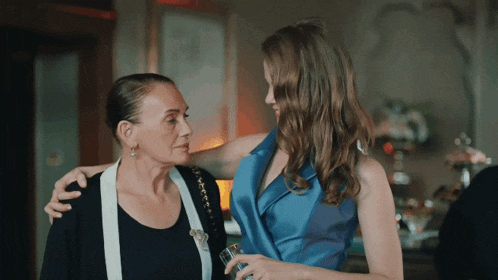 a woman in a blue dress is hugging another woman in a black shirt